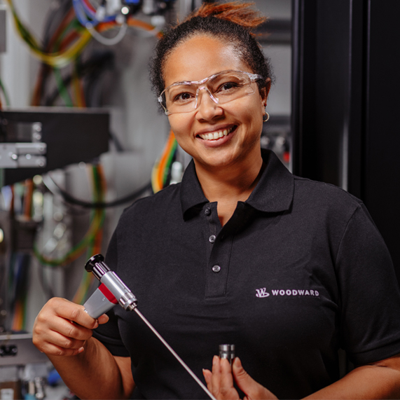 Woodward member woman wearing safety glasses and holding a tool on a manufacturing floor