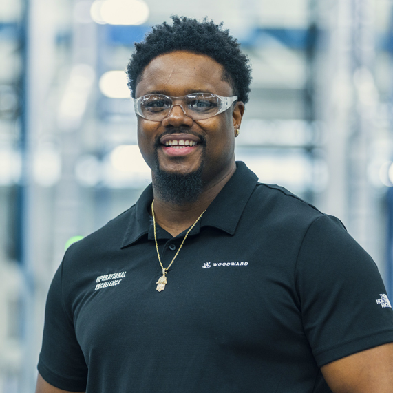 Woodwrd member on manufacturing floor wearing safety goggles in Woodward-branded short